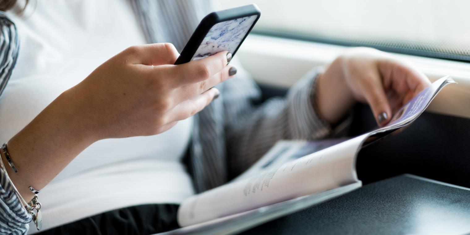 Girl looking at her phone while reading a magazine