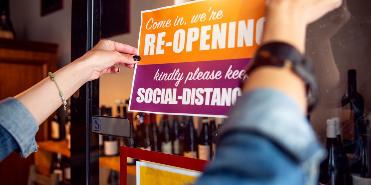 Woman putting up a reopening/social distancing sign 